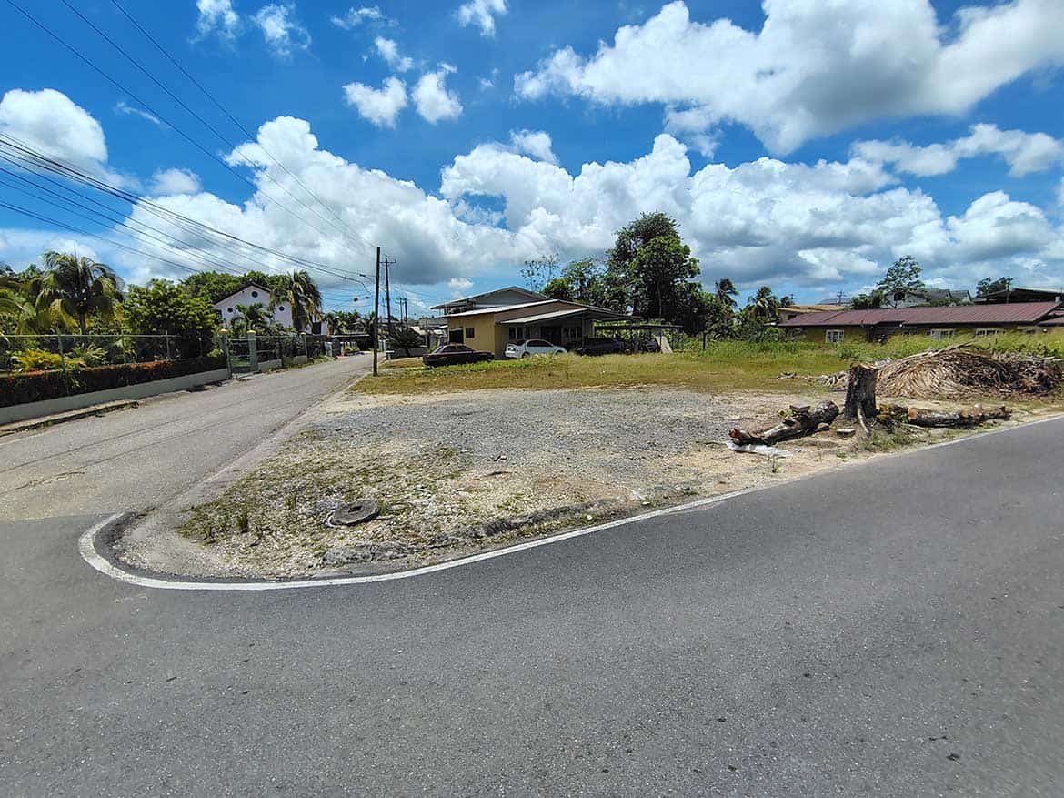 Cornerstone- Empty lot at corner of Ajim Baksh Road with houses and trees nearby.