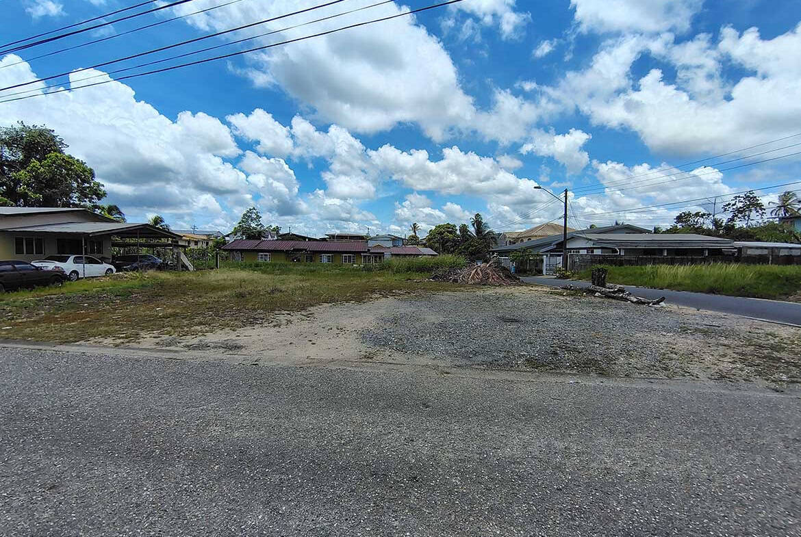 Cornerstone- Open lot on Ajim Baksh Road with houses and power lines under a blue sky.
