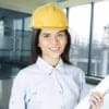 Cornerstone- Female engineer wearing yellow hard hat holding blueprints in modern office.