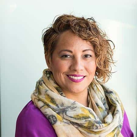 Cornerstone- Smiling woman with curly hair wearing a purple top and scarf.