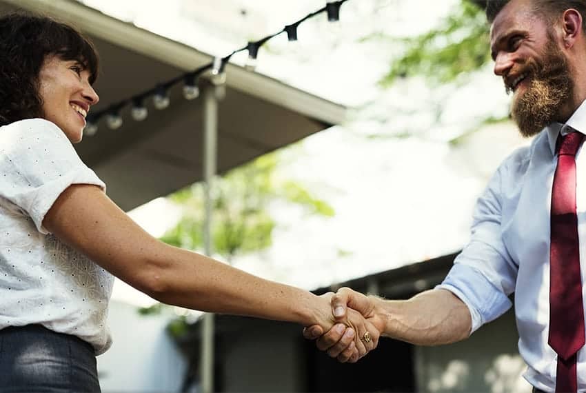 Cornerstone- Realtor shaking hands with a happy client outdoors.