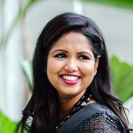 Cornerstone- Smiling woman with dark hair in an outdoor setting with greenery.