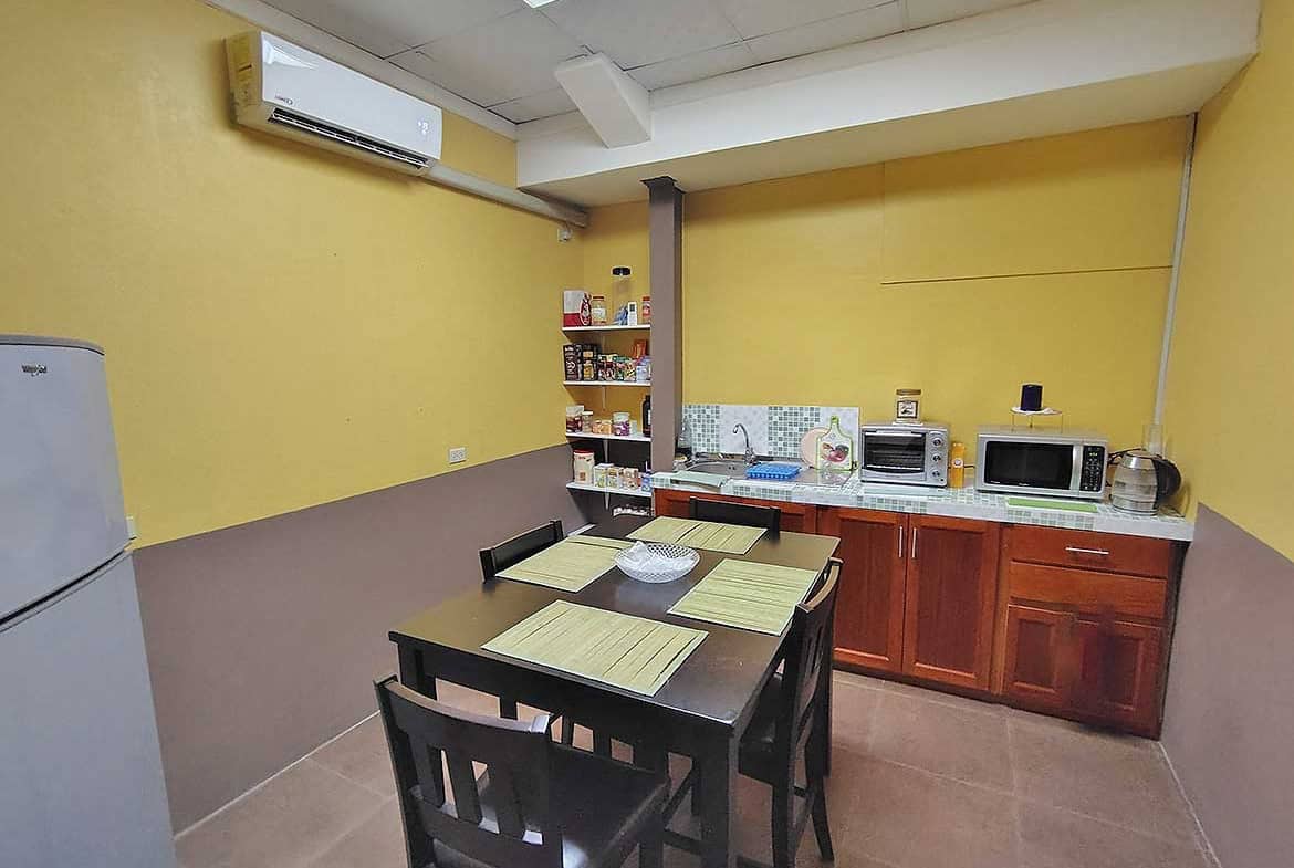 Cornerstone- Office kitchen with yellow walls, wooden cabinets, microwave, and dining table.
