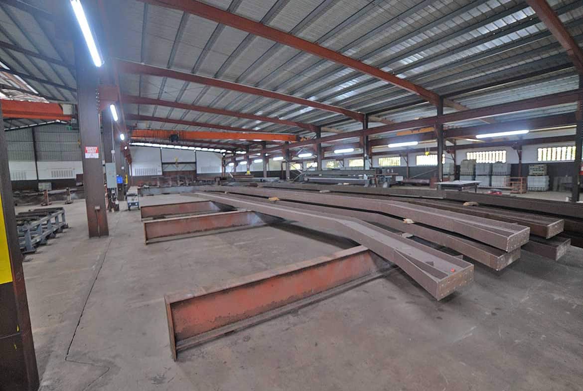 Cornerstone- Large steel beams stored in a spacious industrial warehouse for construction.