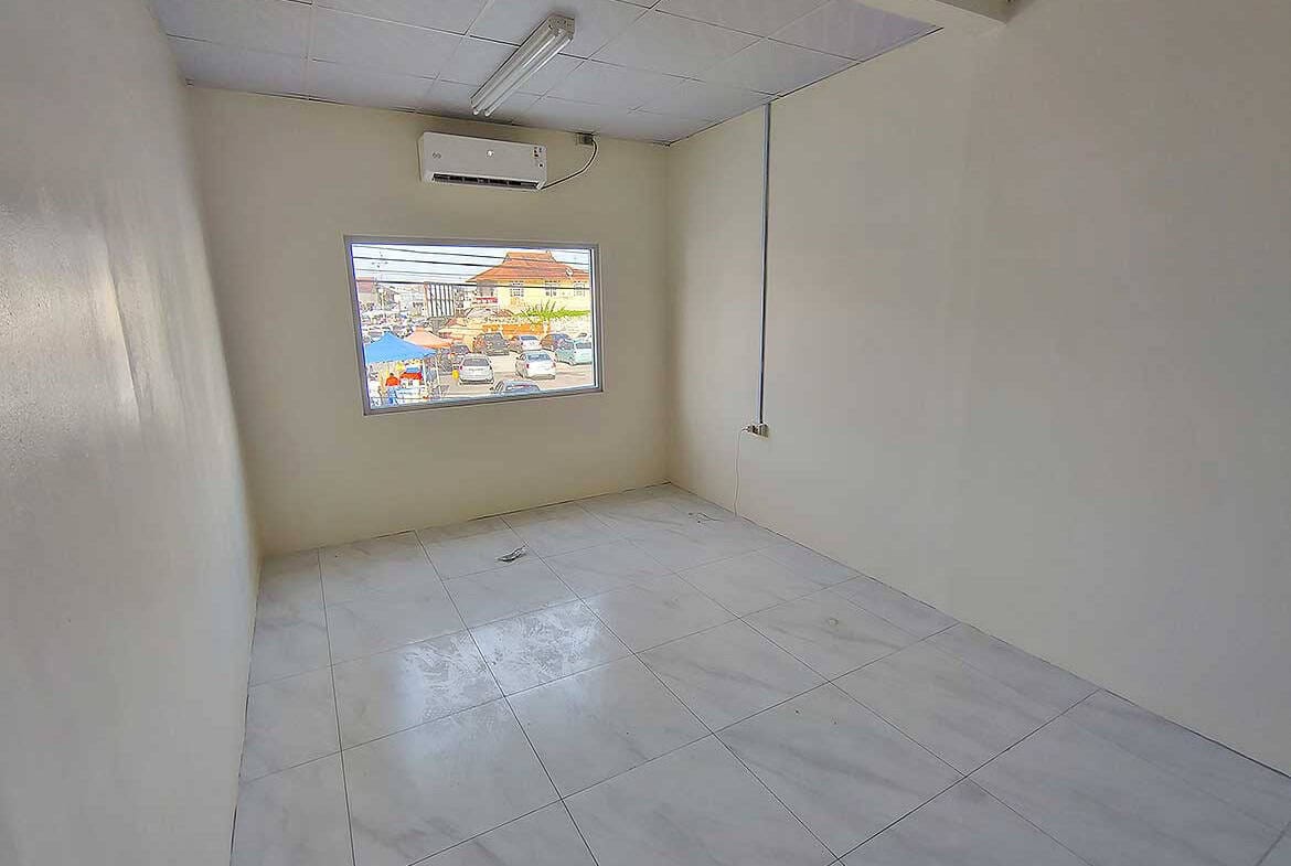 Cornerstone- Empty commercial room with window and air conditioning unit in Curepe.