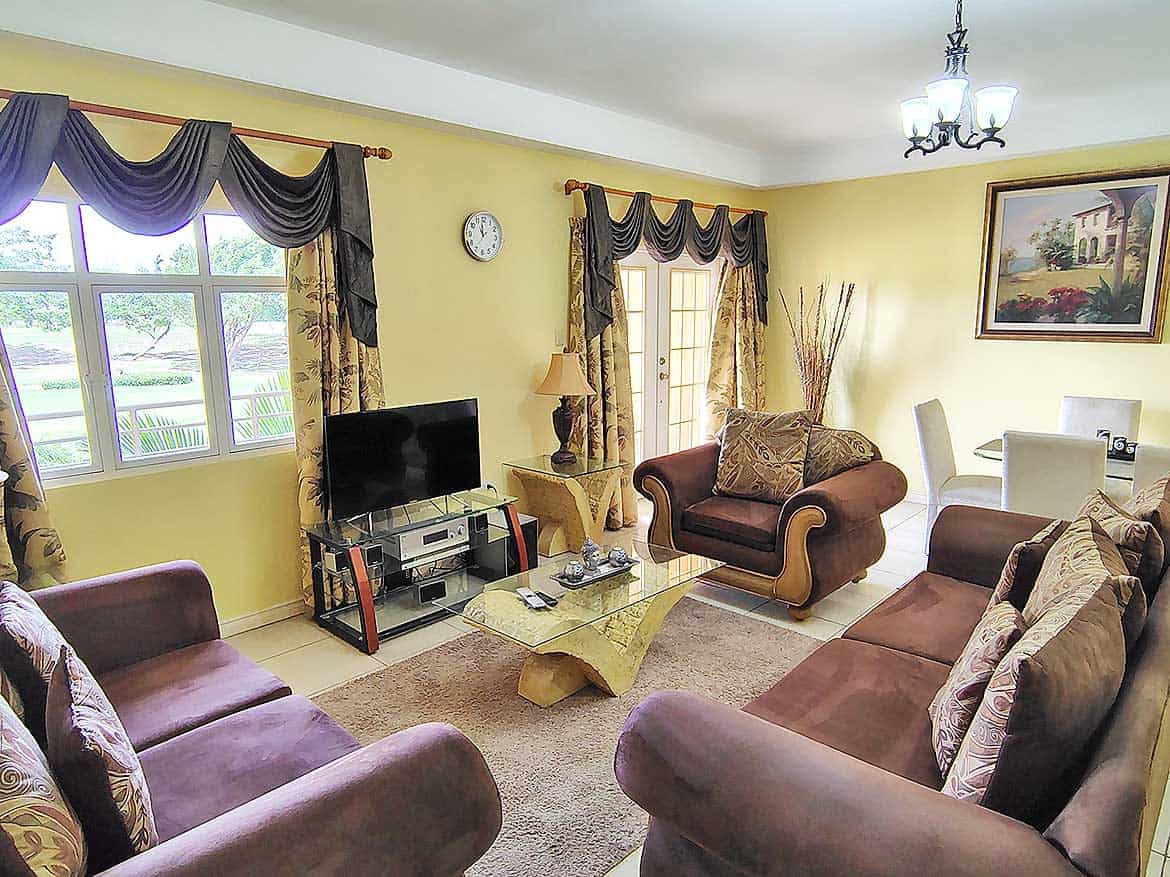 Living Room at EastGate on the Greens Spacious living room with yellow walls, large windows, and elegant furniture.