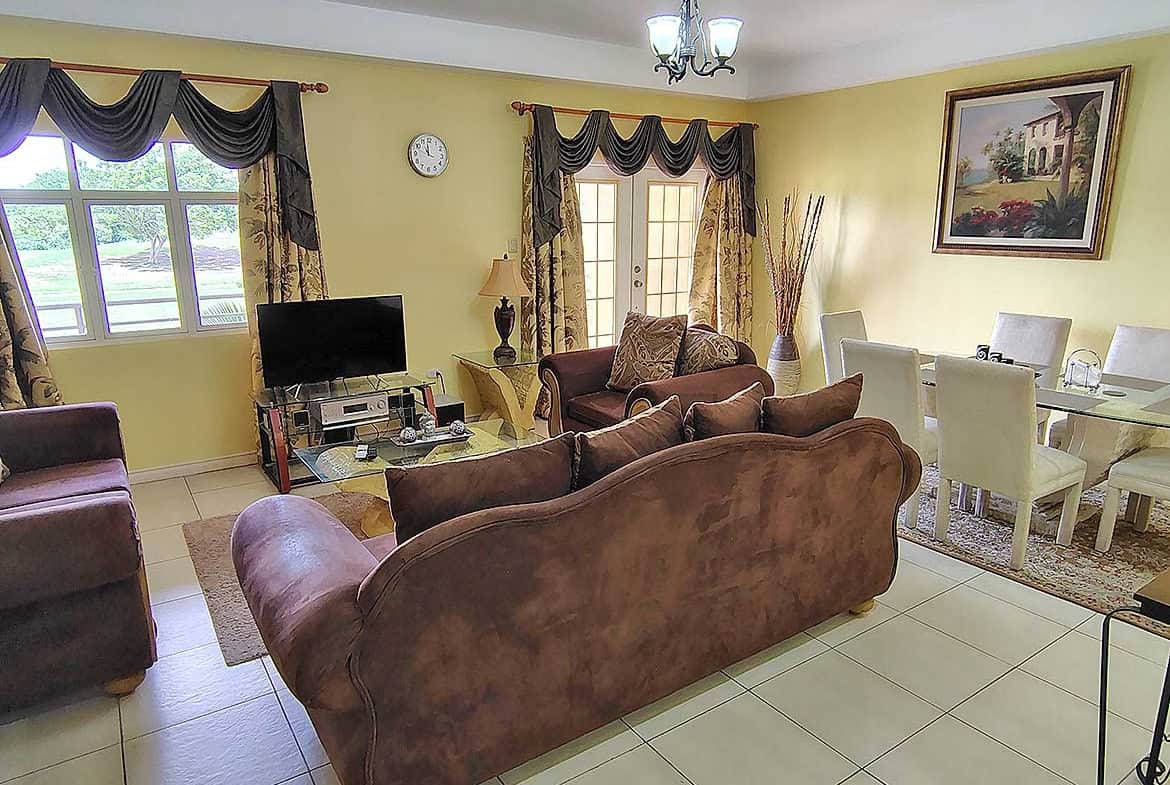 Spacious living room with brown sofas, dining area, and large windows.