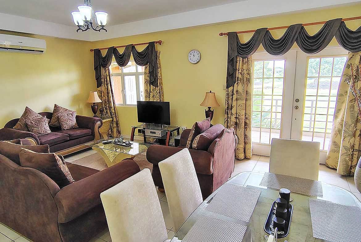 Spacious living room with comfortable sofas, curtains, and a TV in EastGate on the Greens.