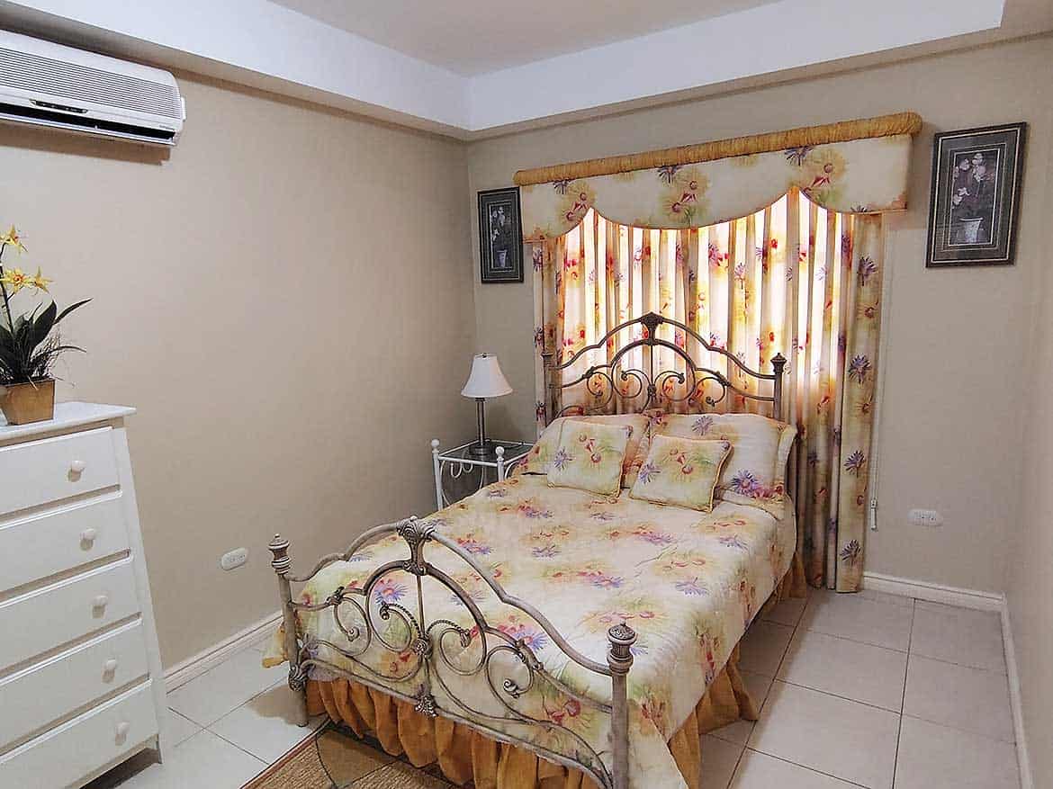 EastGate on the Greens Bedroom Cozy bedroom with floral curtains and vintage bed frame.