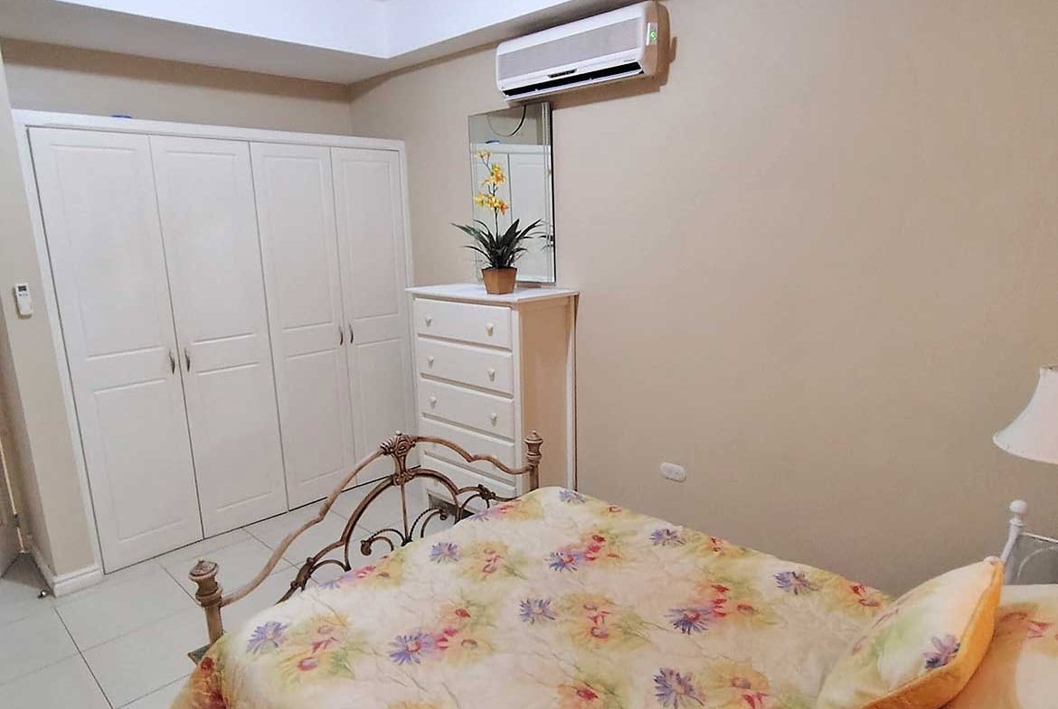 Bedroom with air conditioner, white wardrobe, and floral bedspread.