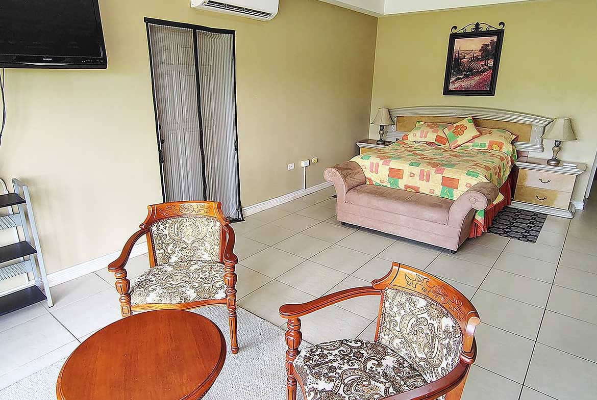 Spacious bedroom with a large bed, two chairs, and a wall-mounted TV.