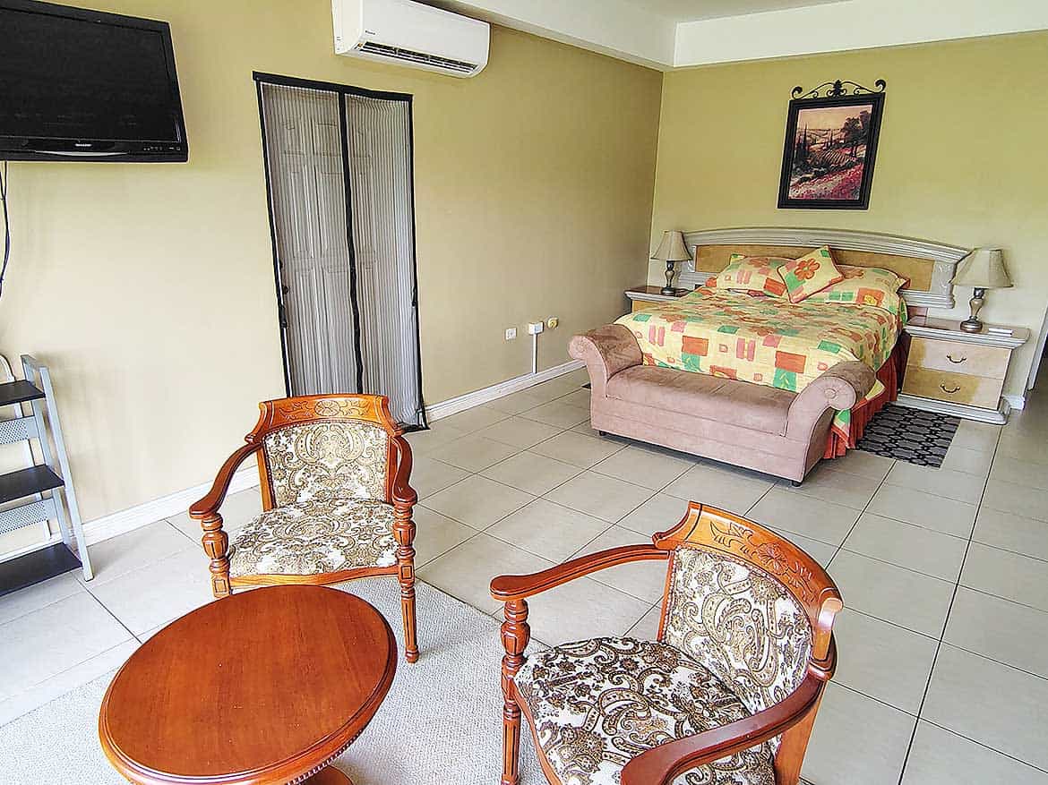 EastGate on the Greens Bedroom Spacious bedroom with a large bed, two chairs, and a wall-mounted TV.