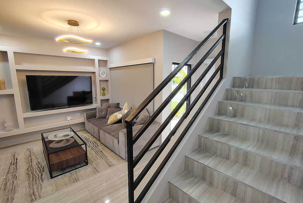 Contemporary living room with TV, sofa, and staircase at Ella Vista Gardens.
