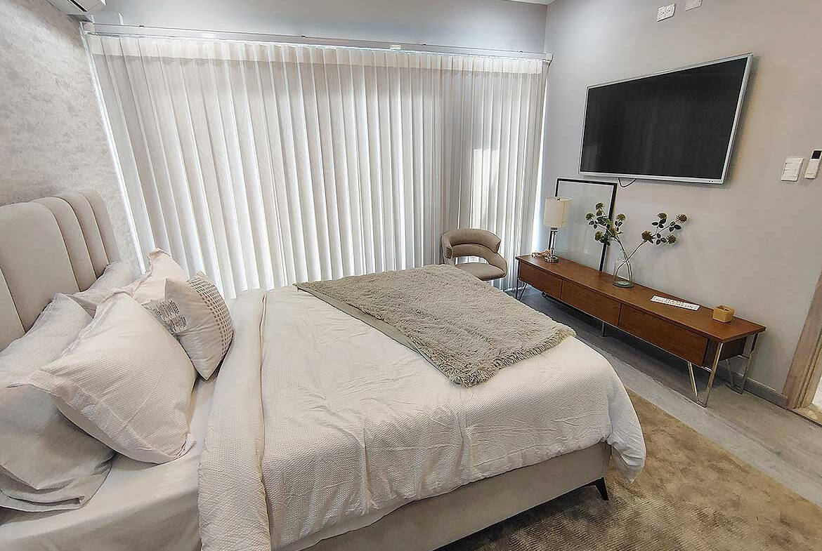 Modern bedroom with large window, TV, and stylish decor at Ella Vista Gardens.