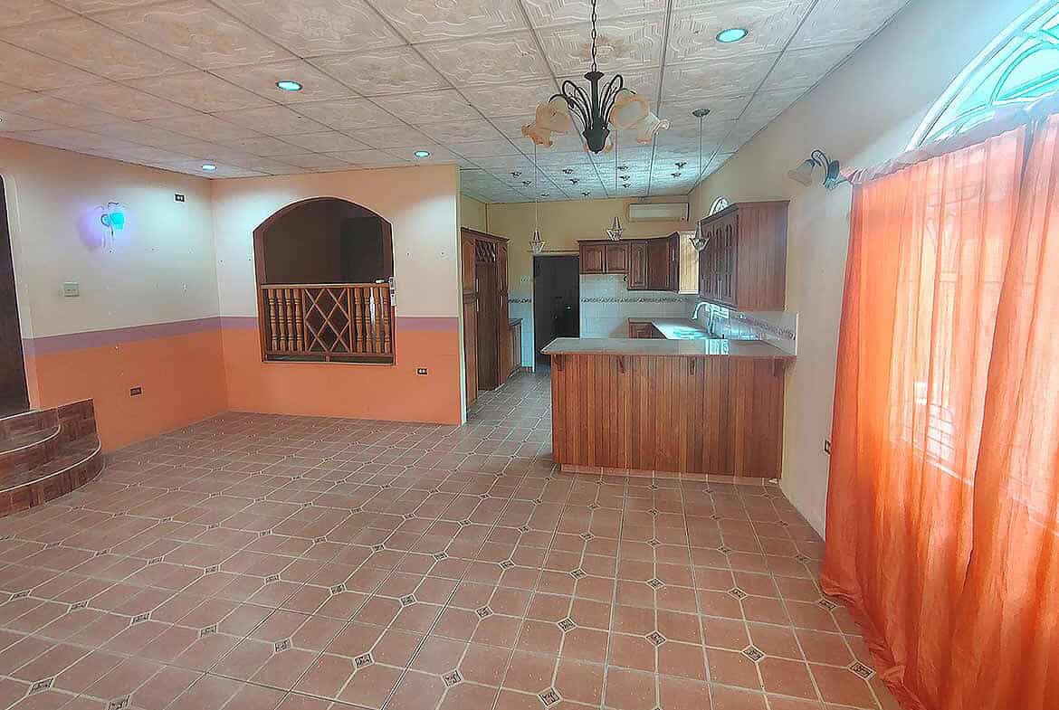 Cornerstone- Bright kitchen and living space with orange curtains and tiled flooring.
