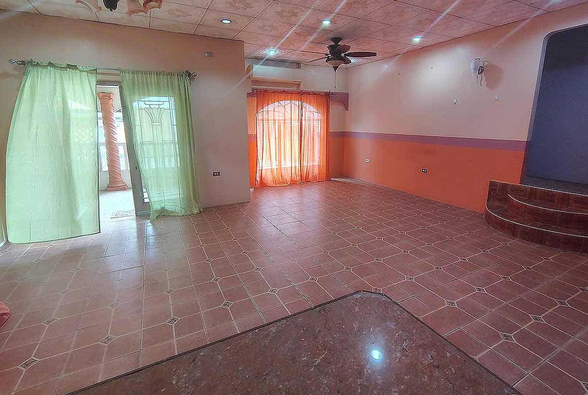 Cornerstone- Bright living room with green and orange curtains, tiled floor, and ceiling fan.