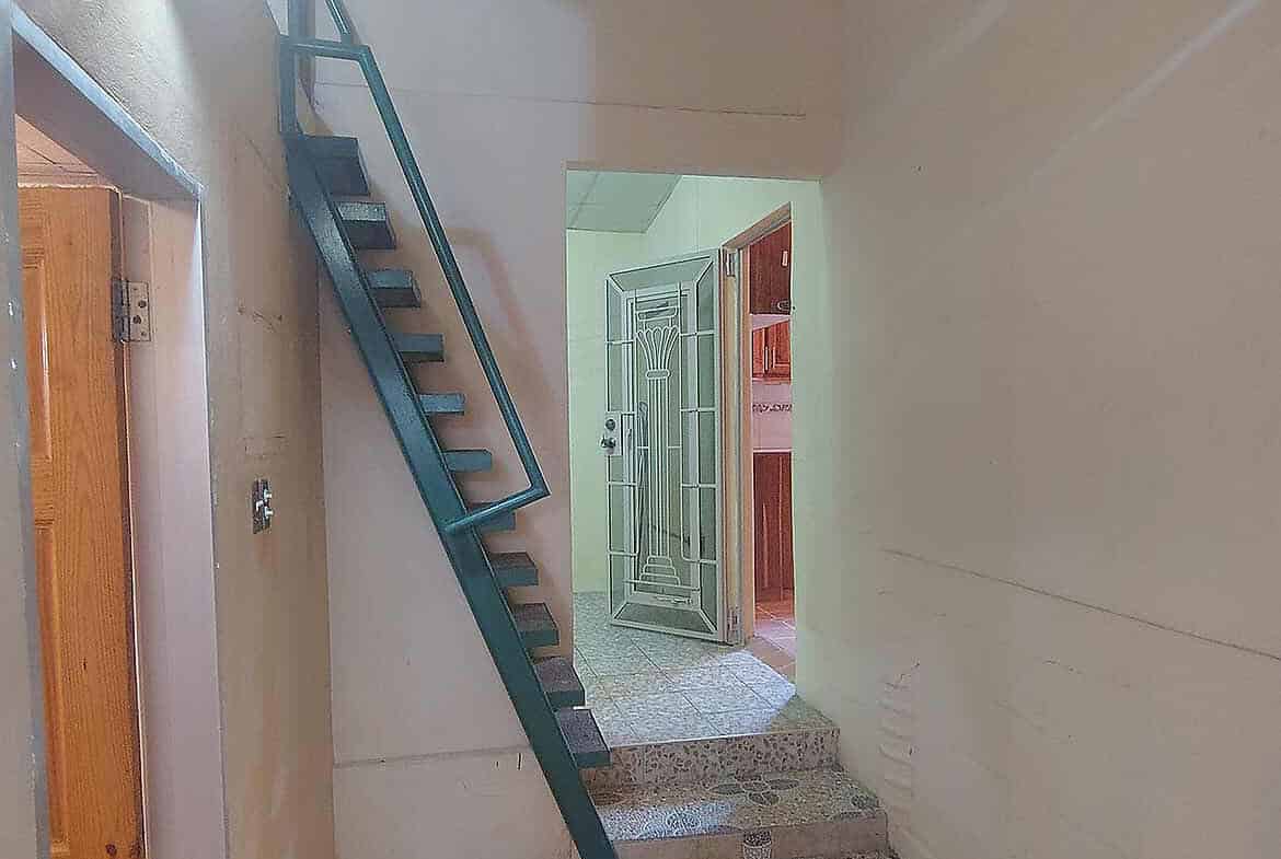 Cornerstone- Indoor staircase with metal railing and open door in the background.
