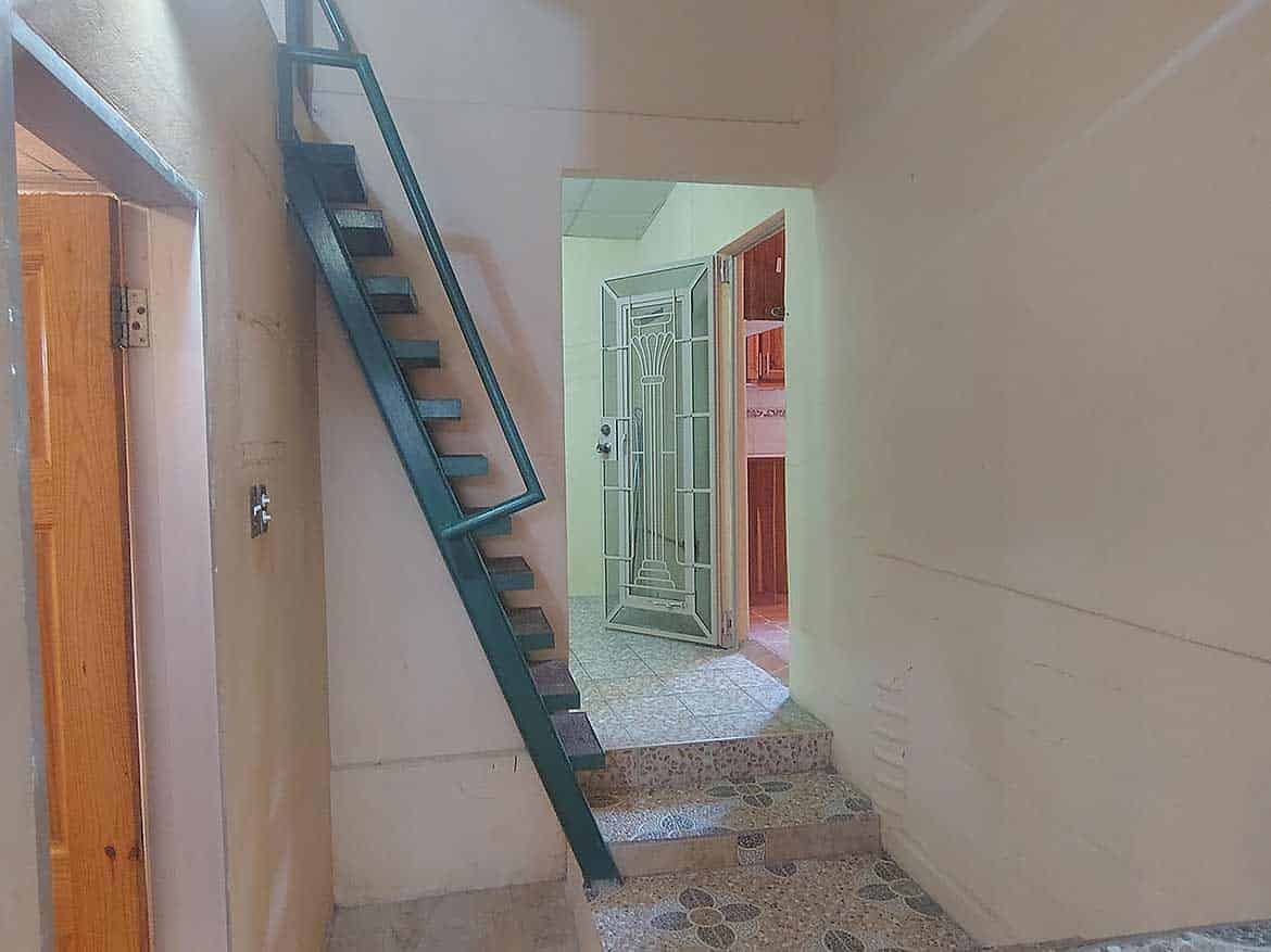 Interior staircase at Cleaver Road, Arima Cornerstone- Indoor staircase with metal railing and open door in the background.