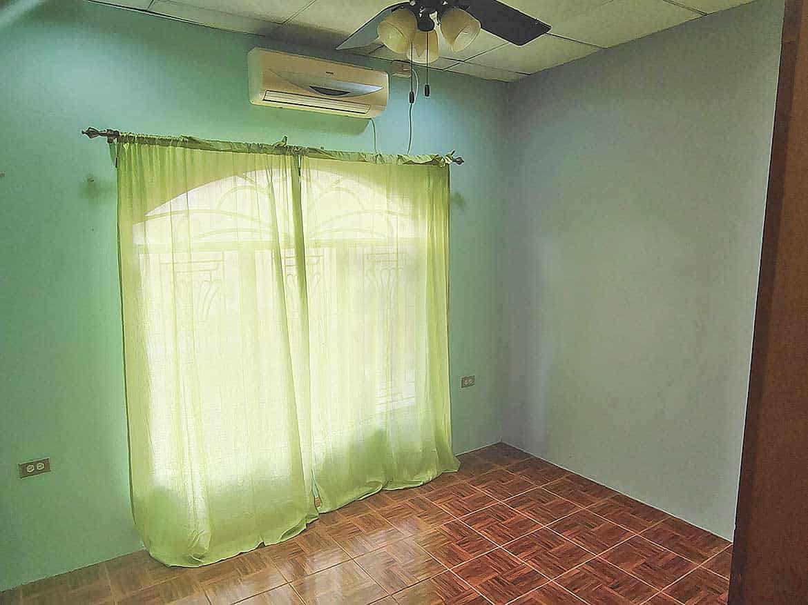 Interior of a Room in Cleaver Road, Arima Cornerstone- Empty room with green curtains, ceiling fan, and air conditioner in Arima.
