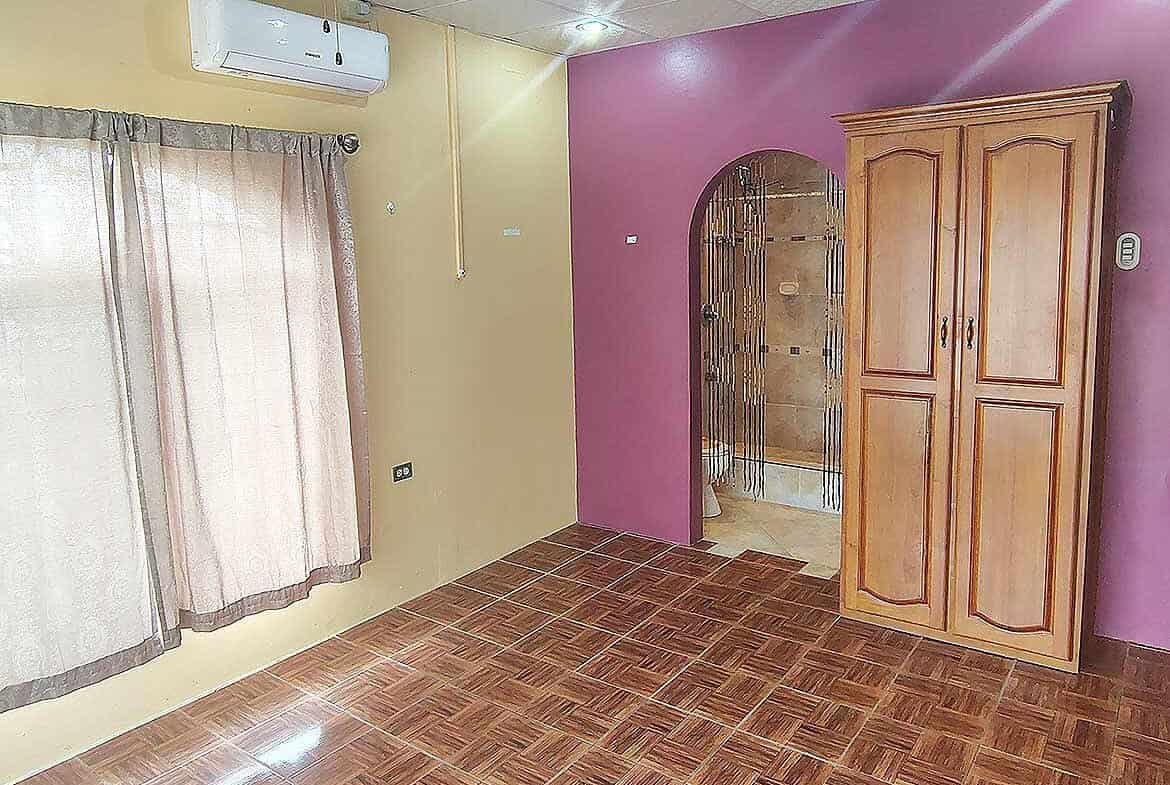 Cornerstone- Room interior with wooden wardrobe, air conditioner, and purple accent wall.