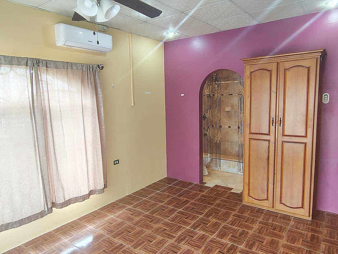 Interior of a Room in Cleaver Road, Arima Cornerstone- Room interior with wooden wardrobe, air conditioner, and purple accent wall.