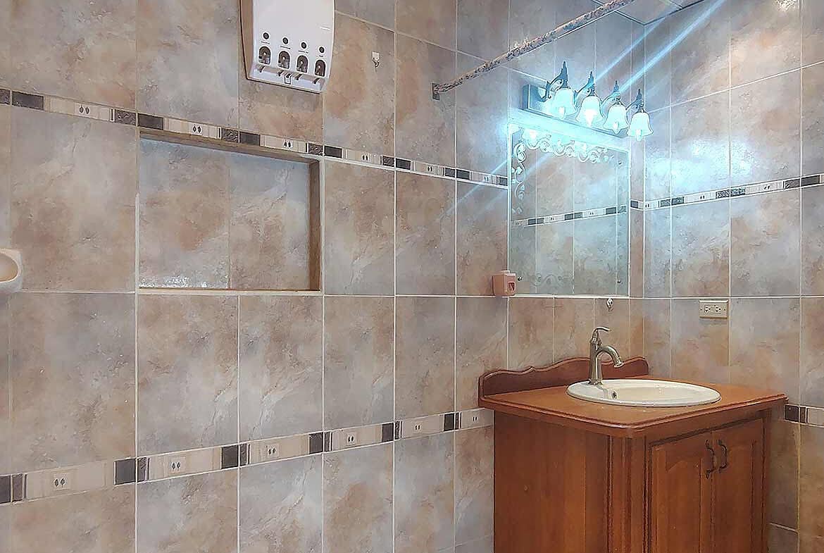 Cornerstone- Bathroom with tiled walls, mirror, and wooden vanity with sink.