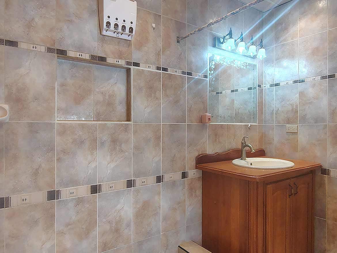 Bathroom with tiled walls and wooden vanity Cornerstone- Bathroom with tiled walls, mirror, and wooden vanity with sink.