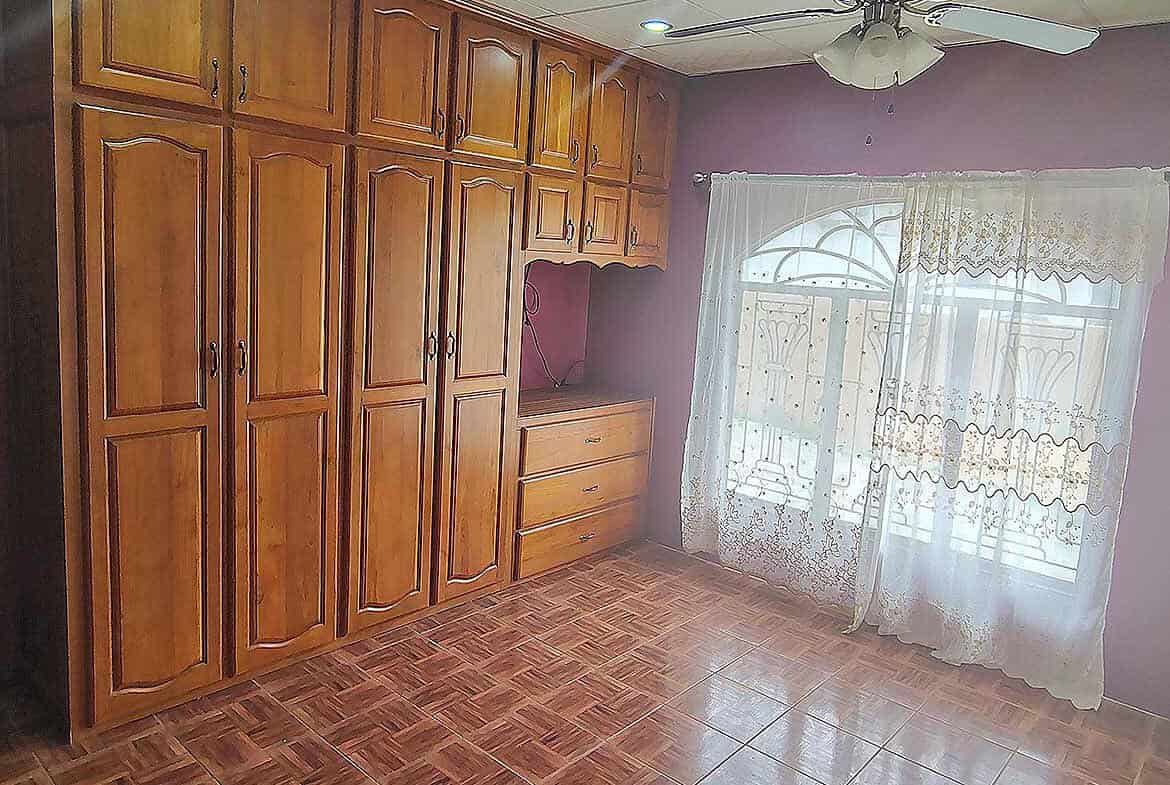 Cornerstone- Spacious room with wooden built-in wardrobes and large window with curtains.