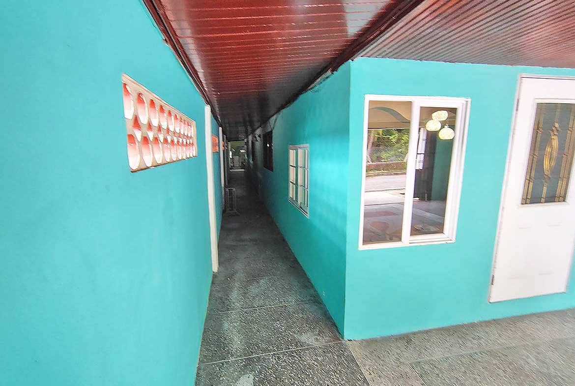 Narrow corridor between turquoise buildings with windows and door.