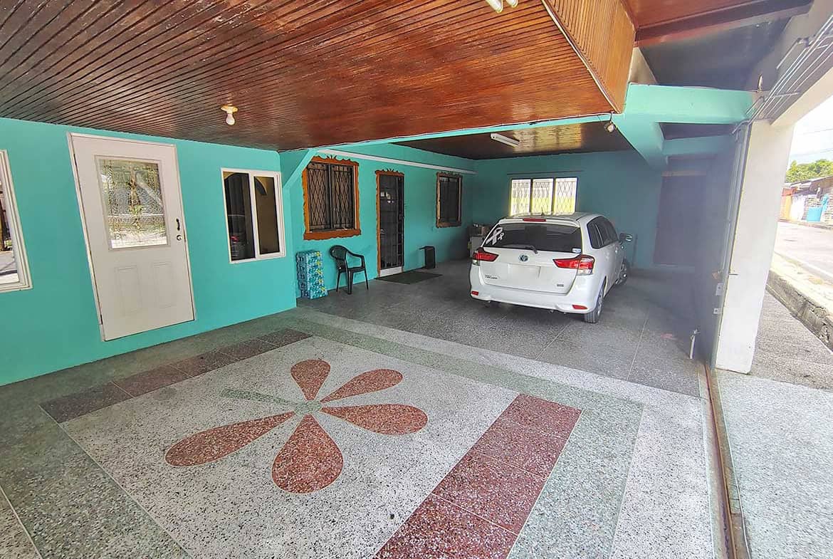 Covered parking space with a white car and turquoise building exterior.