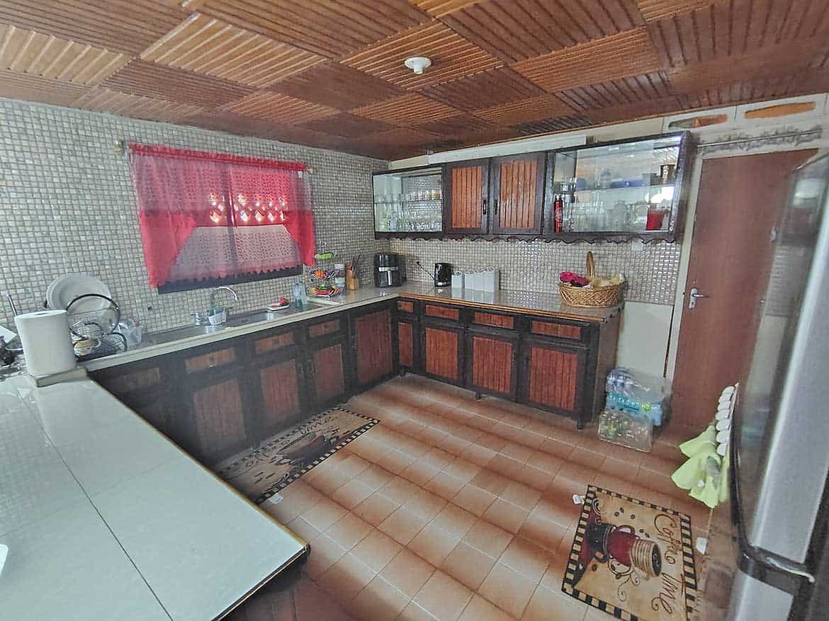 Cornerstone™ Kitchen in Alexander Street Cozy kitchen with wooden cabinets, tiled walls, and a red curtain window.