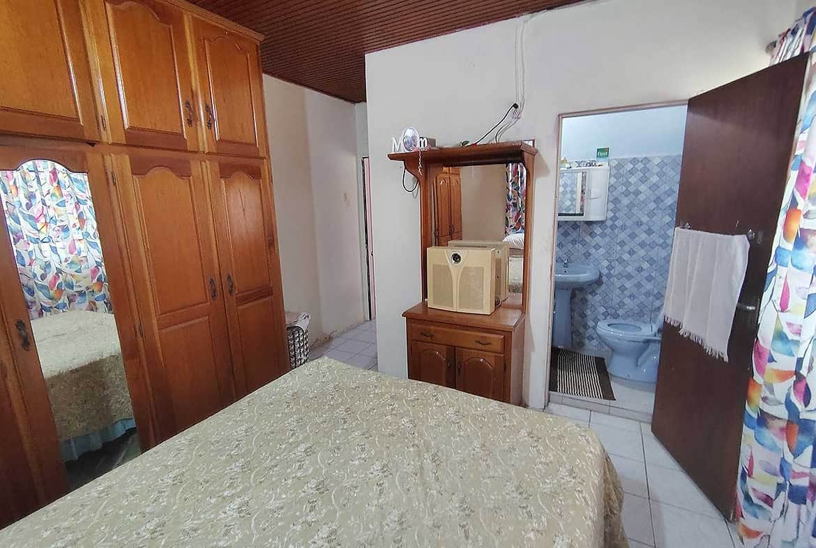 Bedroom with wooden wardrobes, a bed, and a view into the bathroom.