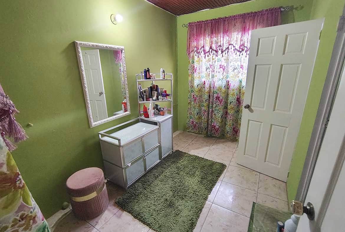 Bright bedroom with green walls, floral curtains, and a mirror.