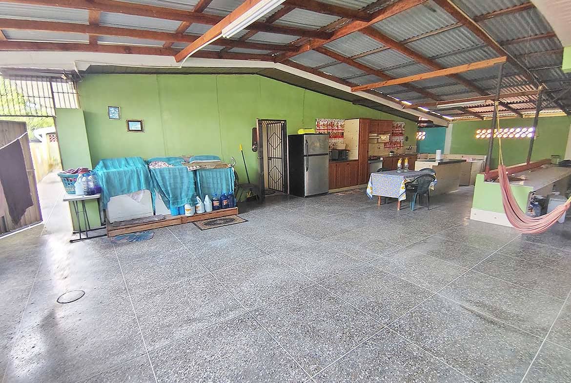 Large open outdoor space with green walls, tables, and a hammock under a metal roof.