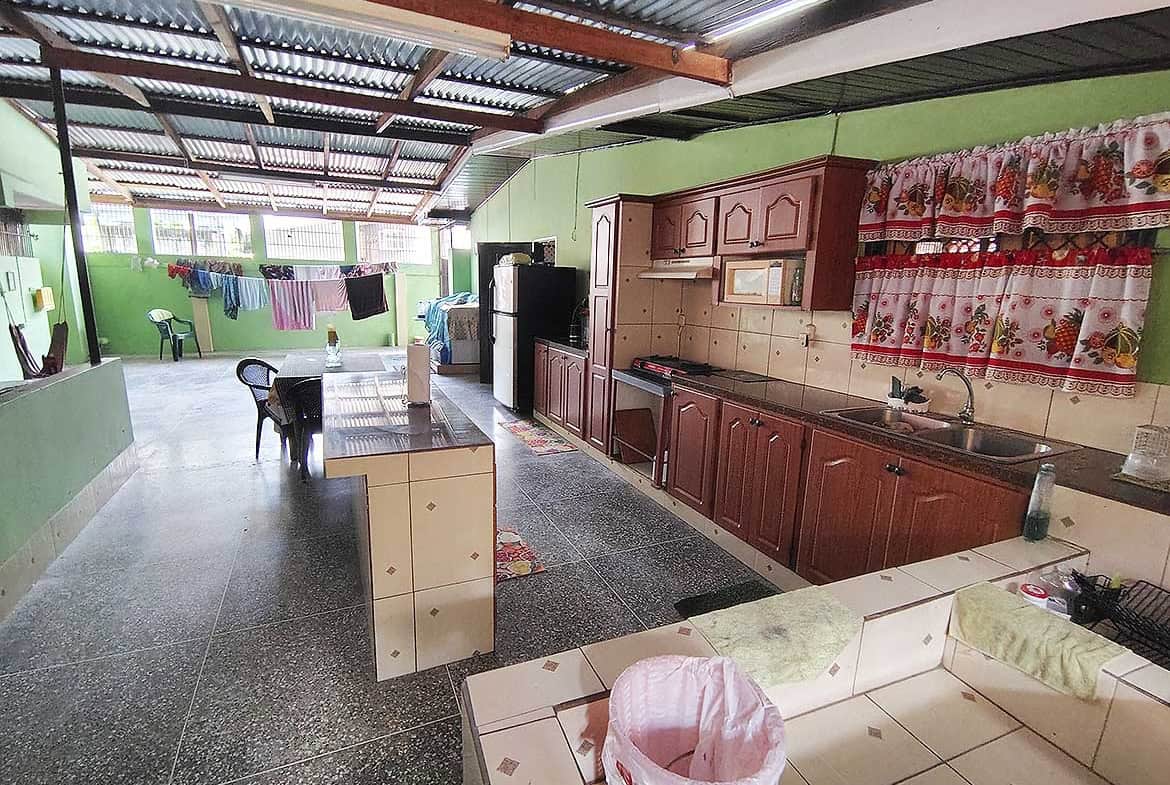 Spacious kitchen with green walls, wooden cabinets, and laundry area in the background.