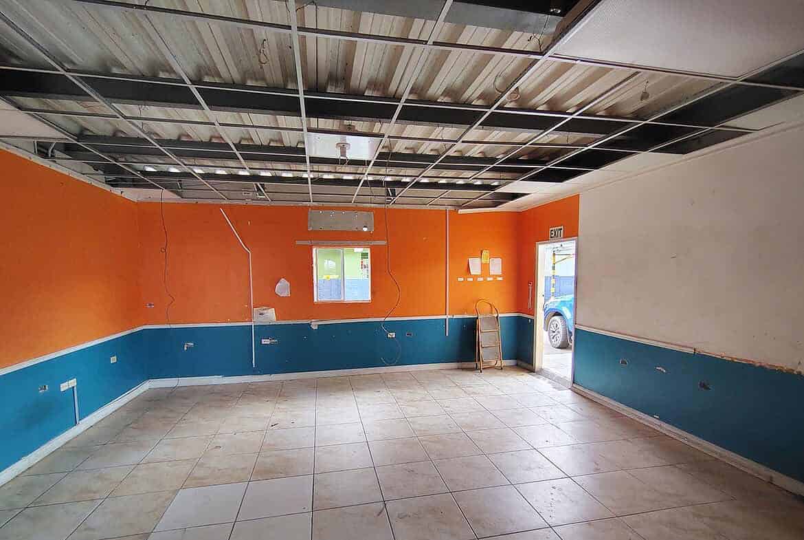 Cornerstone- Empty commercial space with orange and blue walls, tiled floor, and ceiling panels.