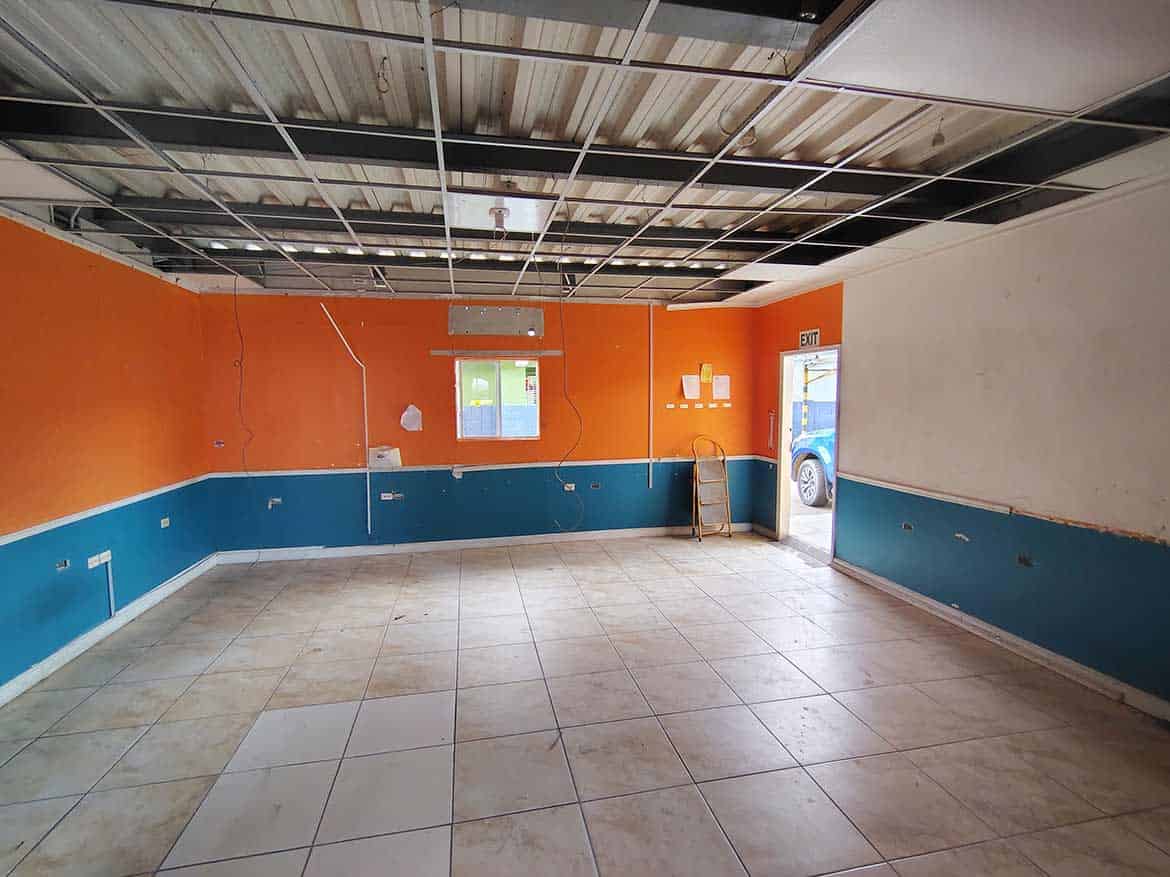 Interior of a Commercial Space for Sale Cornerstone- Empty commercial space with orange and blue walls, tiled floor, and ceiling panels.