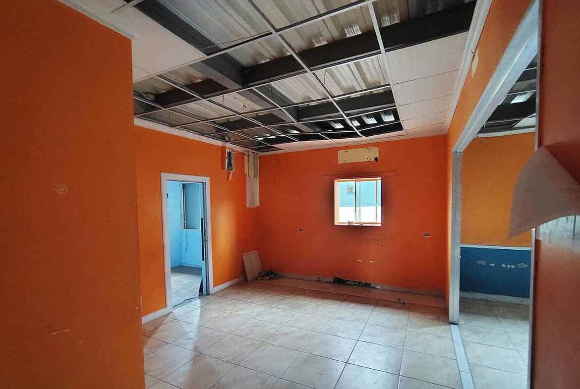 Cornerstone- Empty office room with orange walls and open ceiling panels.