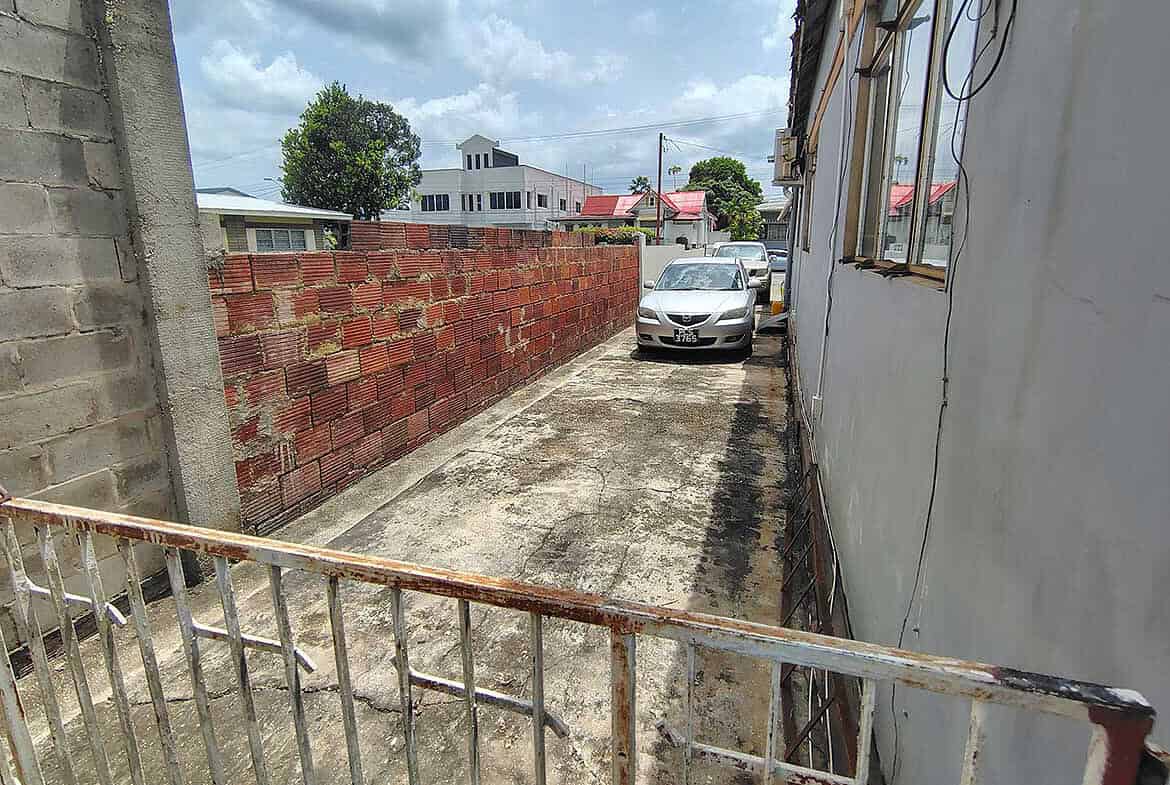 Cornerstone- Empty parking space on Carlos Street in Woodbrook with a parked car and surrounding buildings.