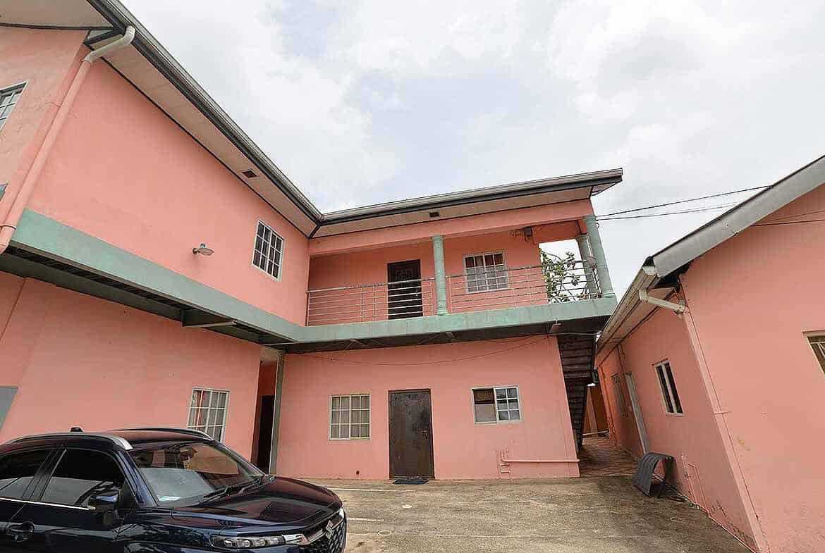 Cornerstone- Pink residential building in Arima with parking area and external staircase.