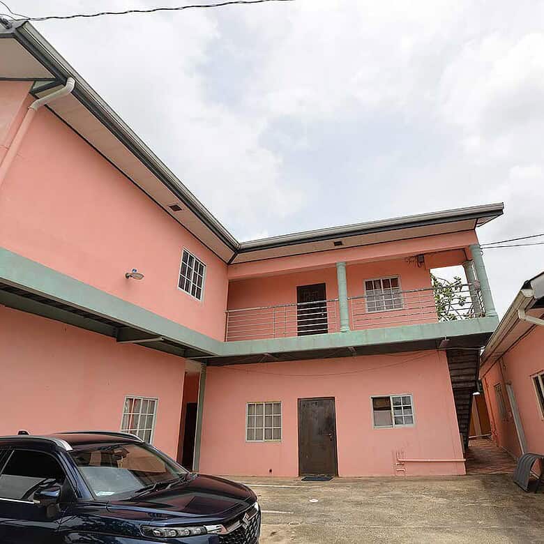 Cornerstone- Pink residential building in Arima with parking area and external staircase.
