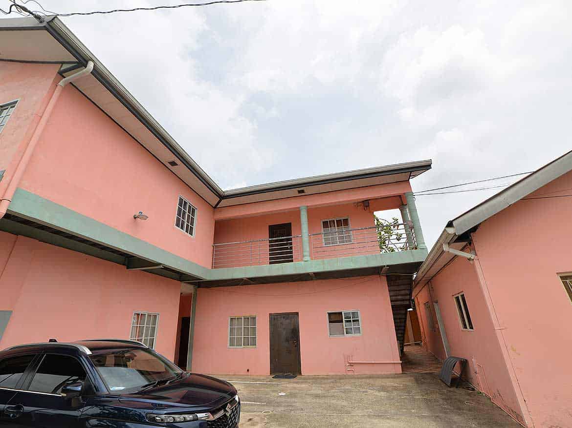 Cornerstone- Pink residential building in Arima with parking area and external staircase.