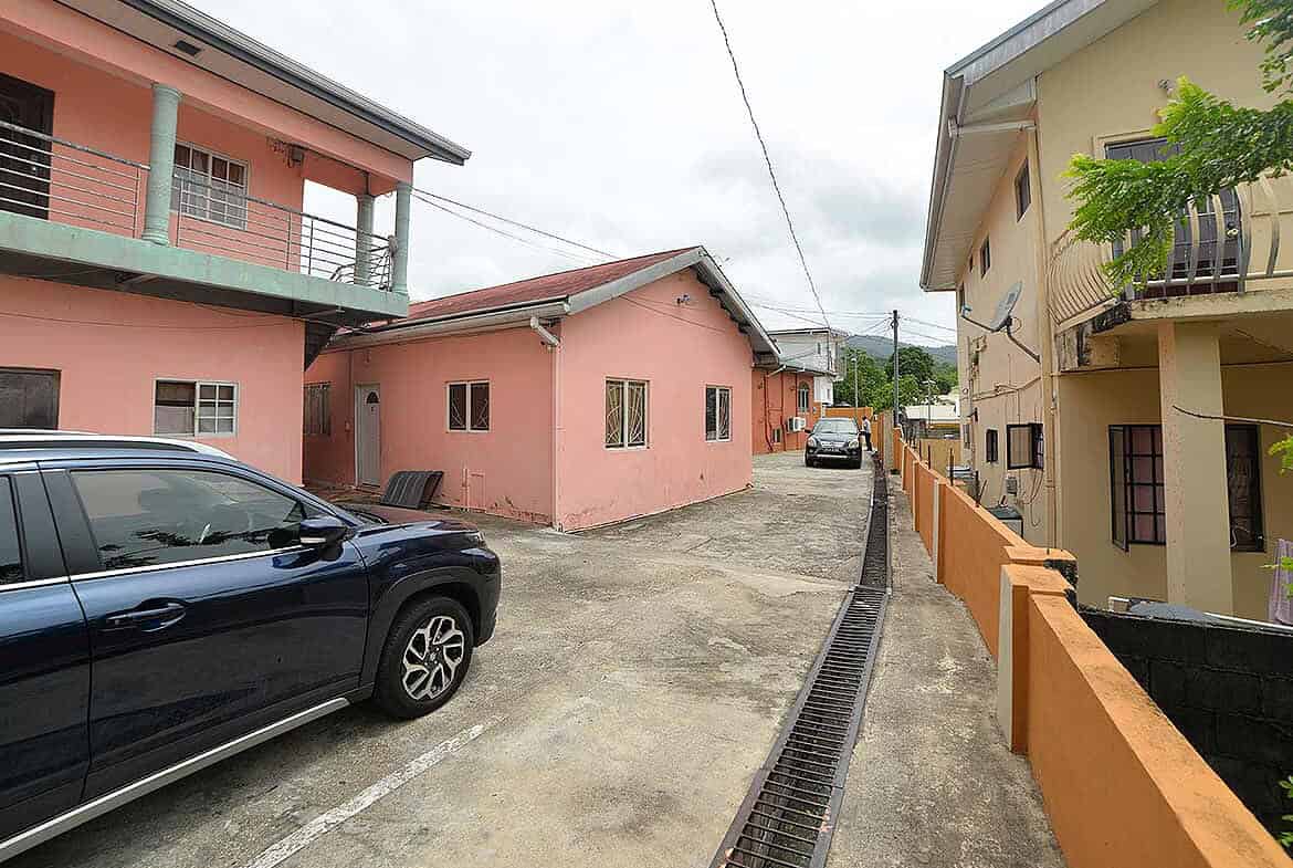 Cornerstone- Colorful houses on Cleaver Road, Arima with parked car and greenery.