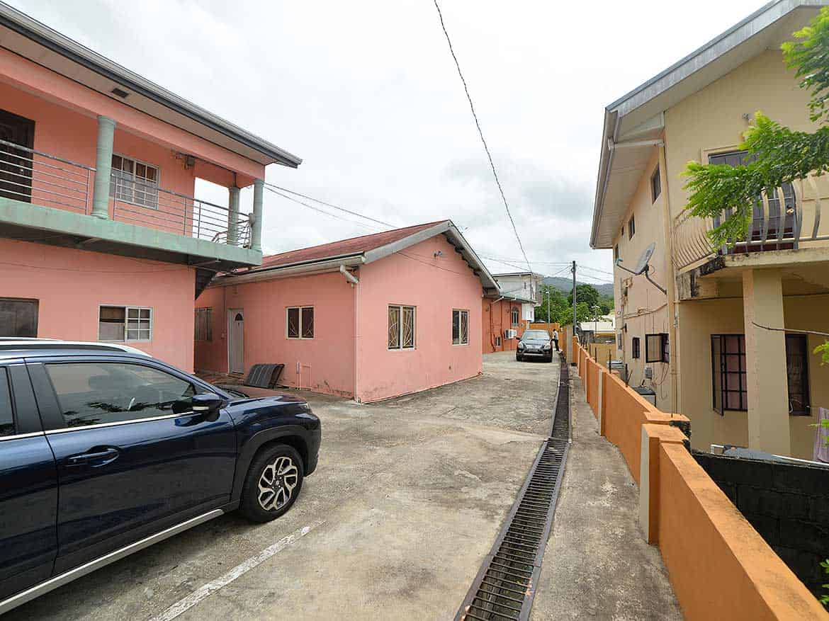 Residential Street in Arima Cornerstone- Colorful houses on Cleaver Road, Arima with parked car and greenery.