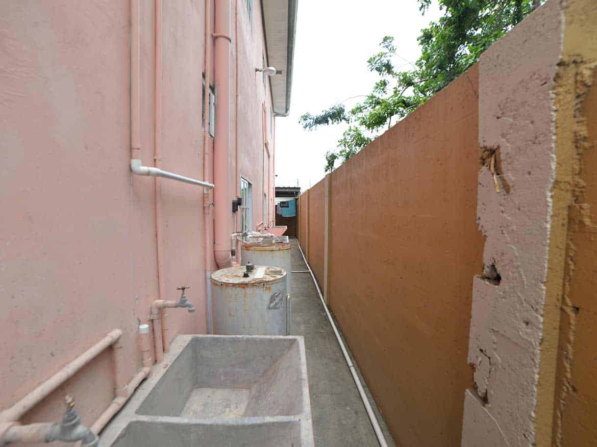Cornerstone™ Cleaver Road Arima Cornerstone- Narrow alleyway with water tanks and a high wall in Arima.