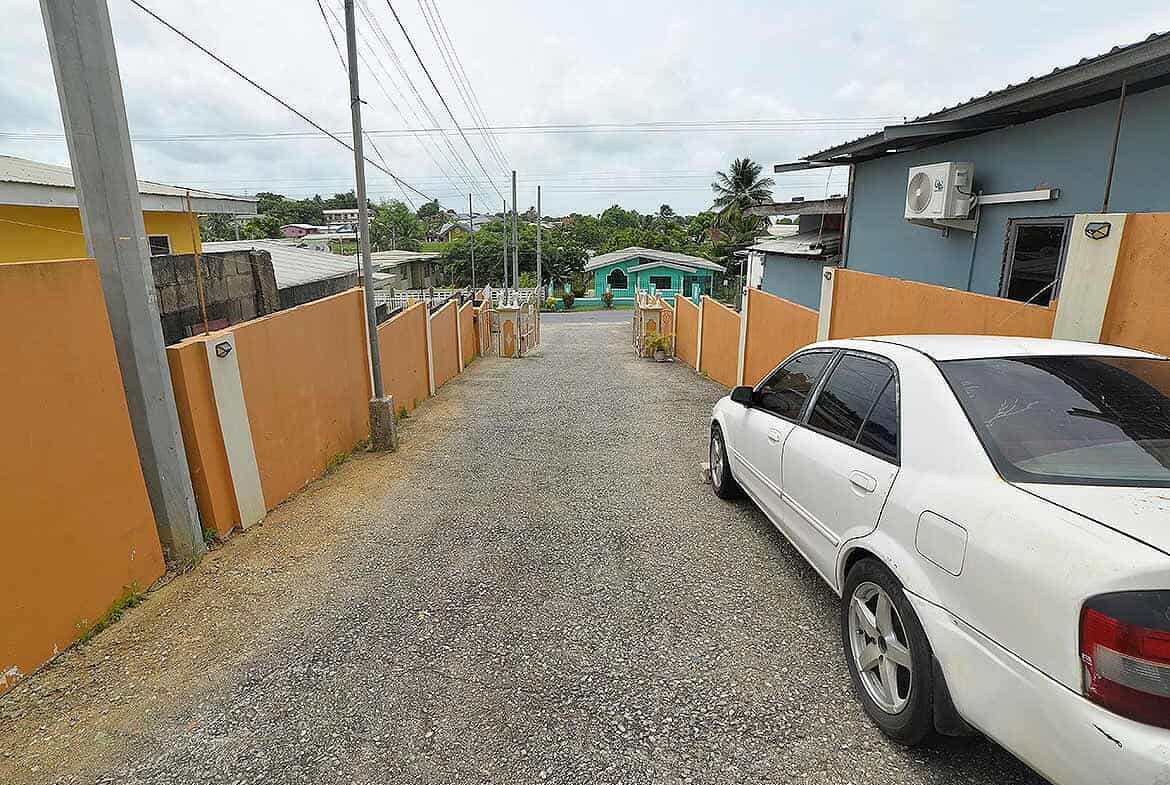 Cornerstone- Residential street view in Arima with parked car and colorful fences.