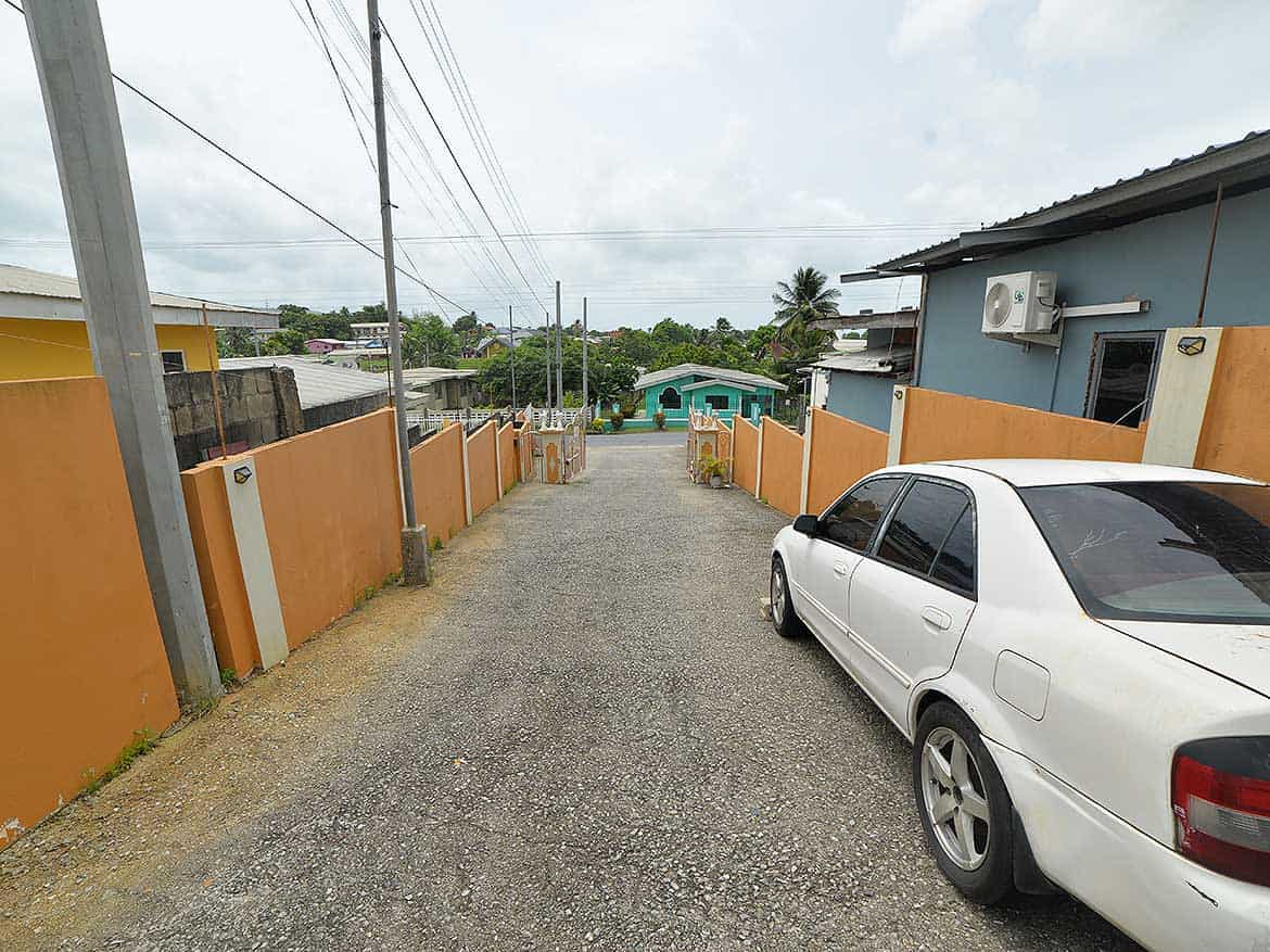 Cornerstone™ Cleaver Road Arima Cornerstone- Residential street view in Arima with parked car and colorful fences.
