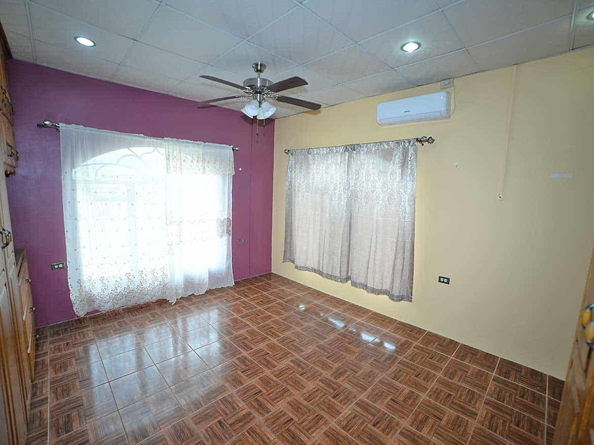 Interior of a Room in Cleaver Road, Arima Cornerstone- Spacious room with purple and yellow walls, ceiling fan, air conditioning, and large windows with dr.