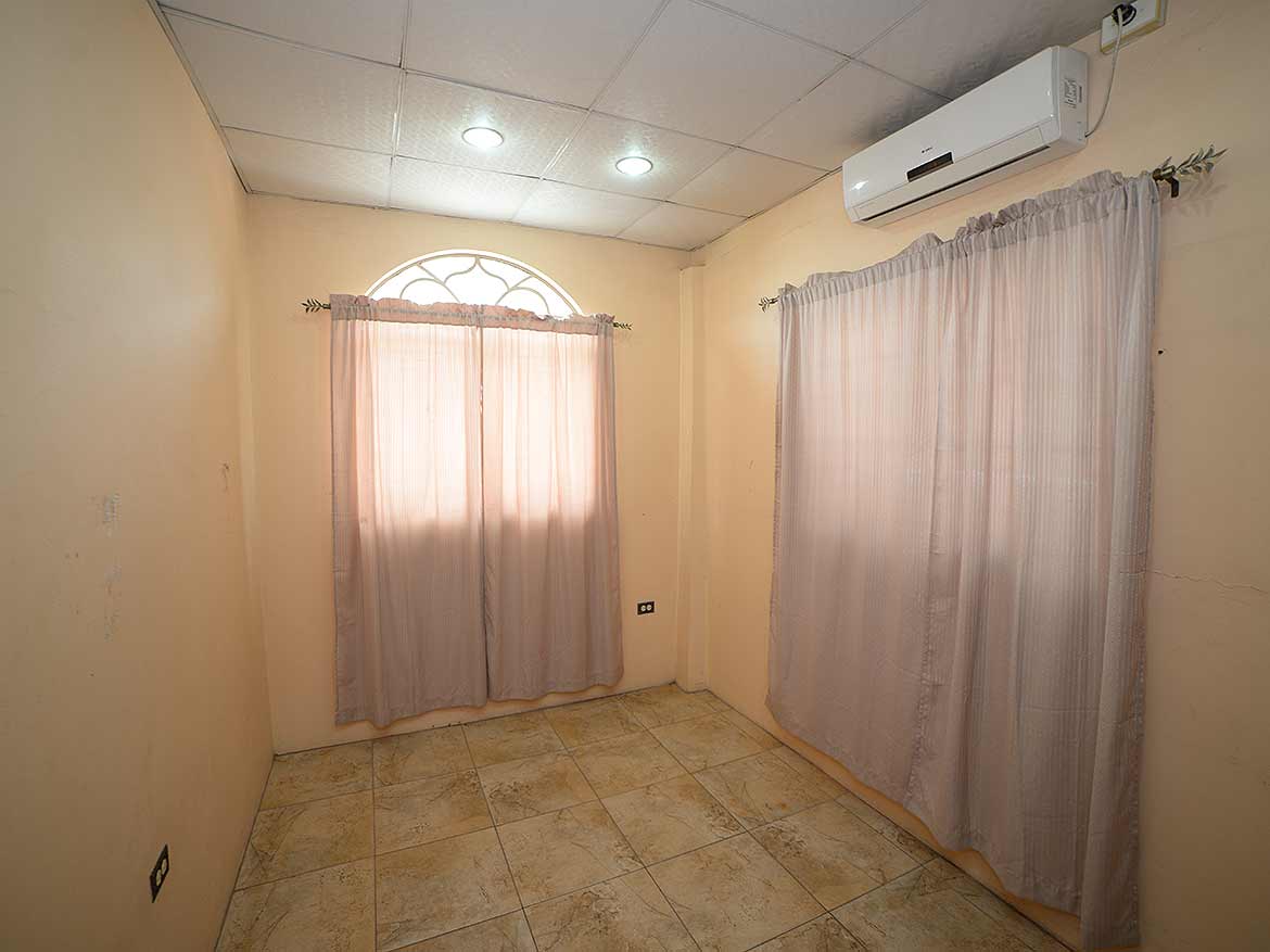 Interior Room with Air Conditioner Cornerstone- Empty room with beige walls, tiled floor, and curtains on windows.