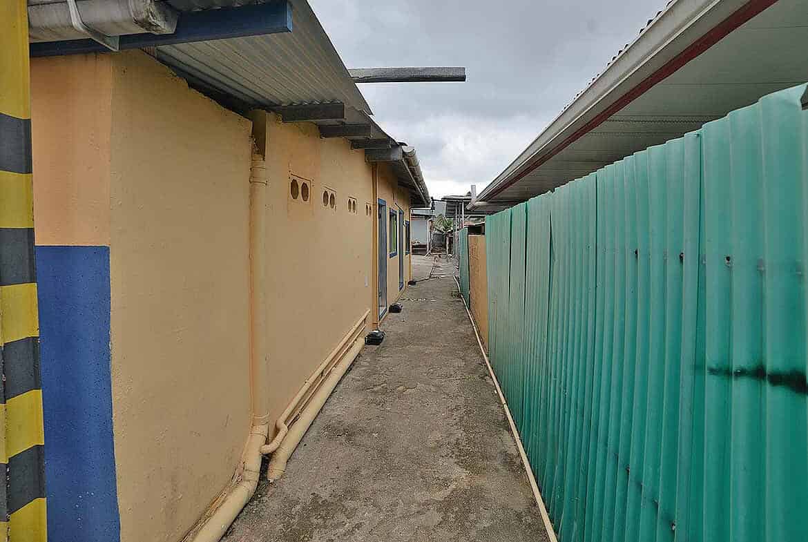 Cornerstone- Narrow alleyway between buildings with corrugated metal fencing.